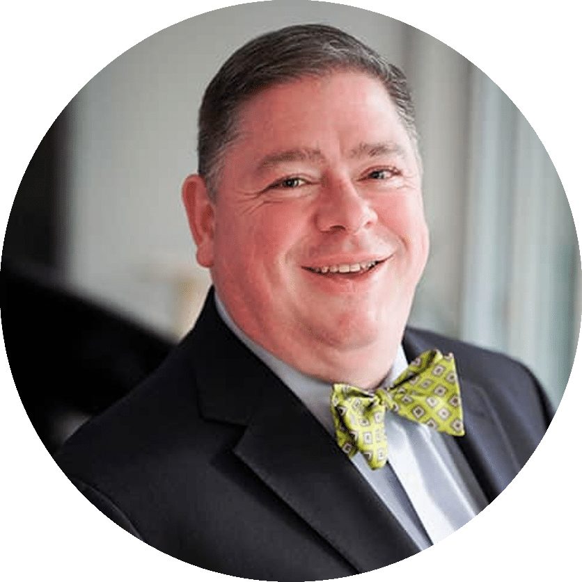 A man in a suit jacket and green patterned bow tie smiles at the camera.